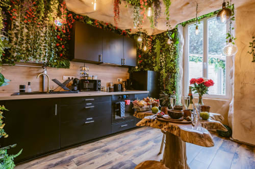 La cuisine Jungle Room des Gîtes De Dordogne avec meubles noirs, plantes suspendues, table en bois et grandes fenêtres