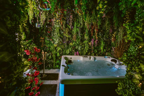 Vue aérienne du jacuzzi spa entouré de plantes verdoyantes et fleurs rouges dans La Jungle Room aux Gîtes de Dordogne