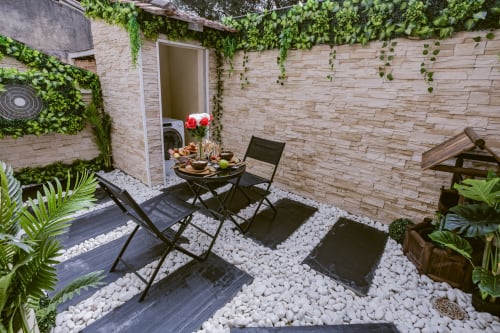 La terrasse extérieure Jungle Room aux Gîtes de Dordogne avec sièges, table à manger, gravier blanc et verdure luxuriante
