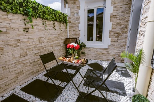 La terrasse de la Jungle Room aux Gîtes De Dordogne avec chaises noires, fleurs rouges et cour en pierre blanche