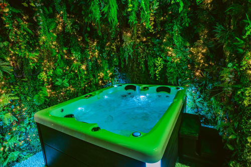 Baignoire ronde aux bordures vertes lumineuses et eau bleue entourée de végétation luxuriante à La Jungle Room, Les Gîtes De Dordogne