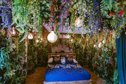La Jungle Room aux Gîtes de Dordogne avec fleurs suspendues, plantes tropicales et lit bleu parsemé de pétales
