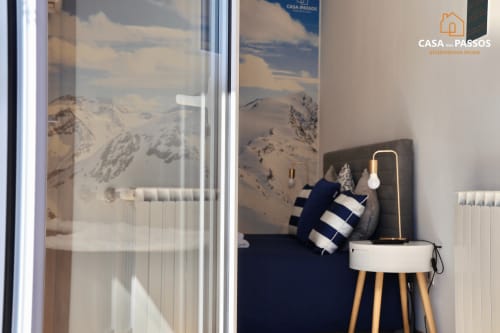 Quarto moderno na Casa Dos Passos em Guarda com arte de montanha nevada, cama azul-marinho com almofada listrada e design minimalista