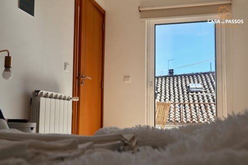Quarto claro com porta de madeira, radiador branco e varanda com vista para os telhados tradicionais de Guarda, Portugal