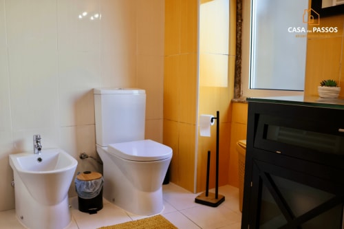 Banheiro moderno com sanitário e bidê brancos, azulejos laranja nas paredes e eletrodomésticos pretos no apartamento Casa Dos Passos em Guarda,