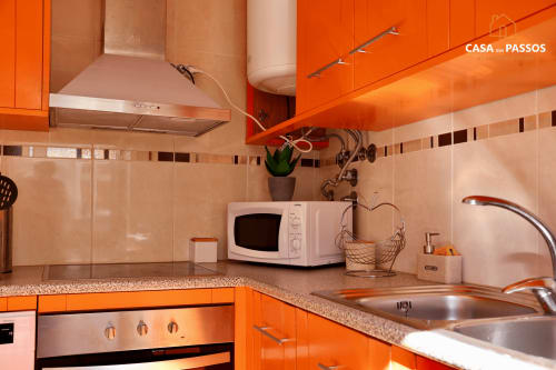 Cozinha moderna no apartamento Casa Dos Passos com armários laranja vibrante, micro-ondas, pia e fogão na SM Stays Collection