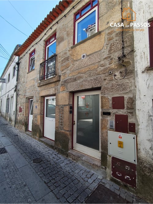 Fachada de edifício histórico em pedra na rua da Guarda, entrada do apartamento Casa dos Passos com janelas de moldura vermelha e porta escura