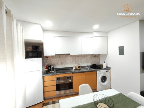 Cozinha moderna no apartamento Casa Dos Passos em Guarda com armários laranja, eletrodomésticos em aço inoxidável e bancadas brancas