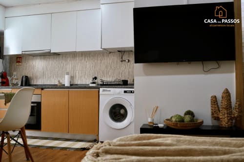 Espaço moderno de cozinha-sala em Casa dos Passos, Guarda, com armários brancos, máquina de lavar, TV e cactos decorativos