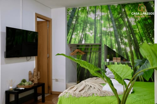 Quarto aconchegante em Casa dos Passos em Guarda com papel de parede floresta de bambu, roupa de cama verde, TV plana e ambiente tropical