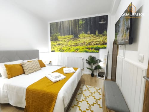 Quarto moderno na Casa Dos Passos em Guarda com destaques em amarelo, TV de tela plana e arte florestal