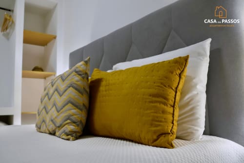 Quarto do apartamento Casa Dos Passos em Guarda com cabeceira cinza, roupa de cama branca e almofadas decorativas amarelas