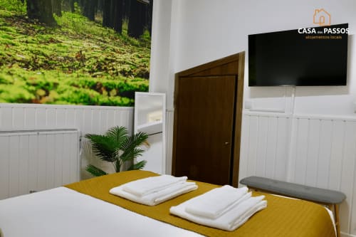 Quarto moderno em Casa Dos Passos em Guarda com colcha amarela, toalhas brancas, porta de madeira escura e TV de ecrã plano