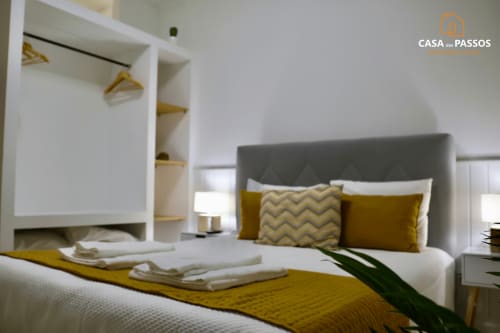 Quarto moderno na Casa Dos Passos com cabeceira cinzenta, almofadas mostarda, roupa de cama branca e roupeiro integrado em Guarda