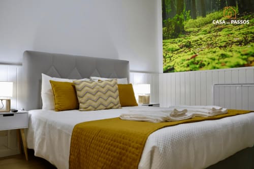 Quarto moderno em Casa Dos Passos em Guarda com cabeceira cinzenta, roupa de cama branca, almofadas douradas e pôster com vista de floresta