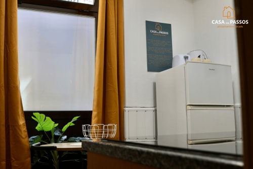 Cozinha americana da Casa Dos Passos com frigoríficos brancos, janela com cortinas douradas, planta e placa informativa em Guarda,