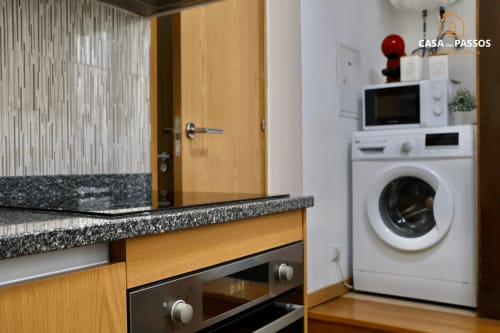 Cozinha moderna com bancada em granito, armários de madeira e máquina de lavar branca no apartamento Casa Dos Passos, Guarda