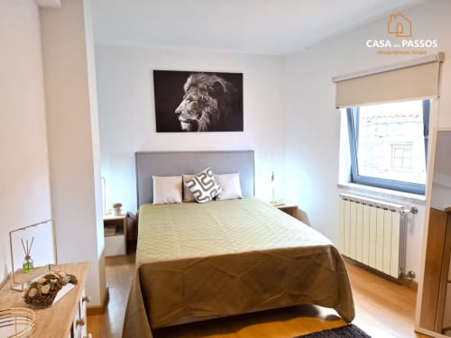 Quarto luminoso na Casa Dos Passos em Guarda com cama queen, arte com leões, janela com vista para a cidade e comodidades modernas