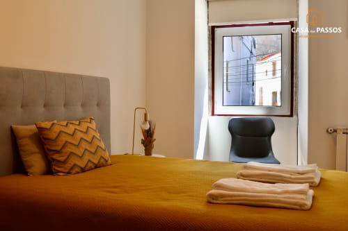 Quarto aconchegante da Casa Dos Passos em Guarda com roupa de cama amarela, cabeceira bege e vista para a cidade