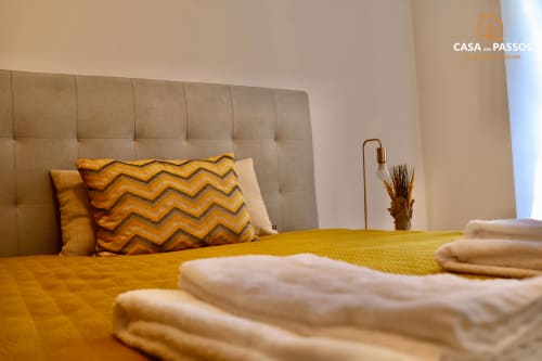Quarto elegante na Casa Dos Passos, Guarda com almofada chevron amarela, cabeceira estofada bege e roupas de cama dobradas