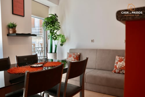 Apartamento Casa dos Passos em Guarda com mesa de jantar, sofá bege, detalhes em laranja, plantas e varanda com vista da cidade