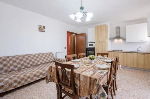 Open-plan apartment in Como with dining table, wooden chairs, sofa, kitchen, and mountain views at Residenza Vecchio Faggeto