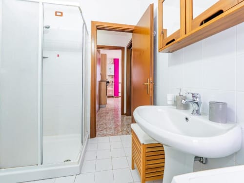 Modern bathroom with white sink, wooden vanity, glass shower enclosure, and wooden cabinets at Como Holiday apartment in