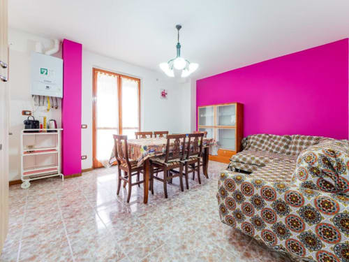 Bright apartment living room in Como with vibrant pink accent wall, wooden dining table, patterned sofa, and mountain views