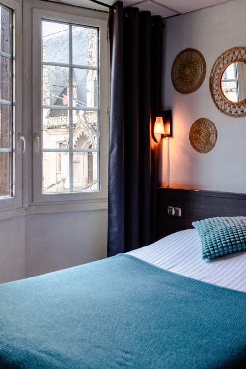 Chambre moderne à l'Hôtel les Initiés à Rouen avec literie turquoise, décoration murale tissée et fenêtres donnant sur le Palais de