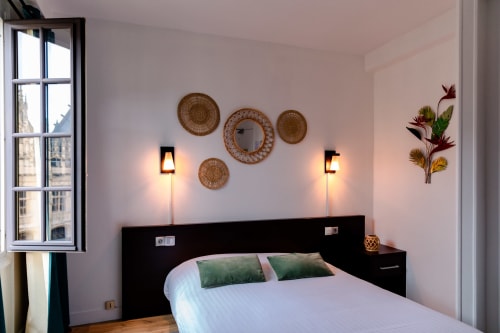 Chambre moderne à l'Hôtel les Initiés à Rouen avec lit queen-size, décoration murale tissée et lampes de lecture en laiton