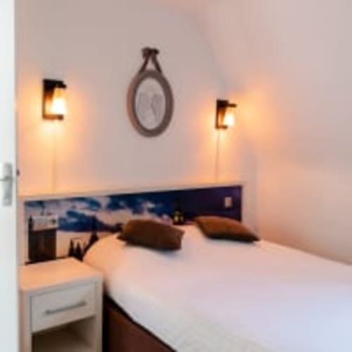 Modern bedroom at Hôtel les Initiés in Rouen with double bed, wall sconces, clock, and ocean-view headboard