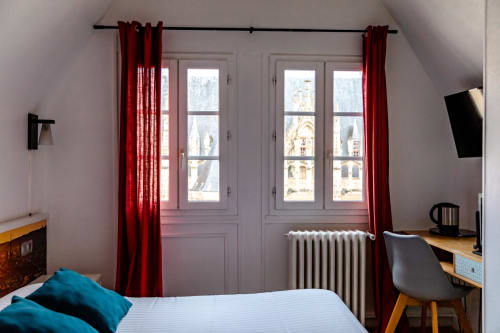 Chambre mansardée lumineuse à l'Hôtel les Initiés à Rouen avec rideaux rouges, bureau et vue sur le Palais de Justice