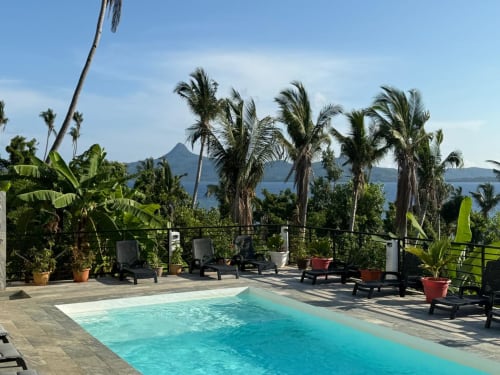 Terrasse de la piscine Le Chissioua avec palmiers et vue sur l'océan surplombant le paysage volcanique de Sada