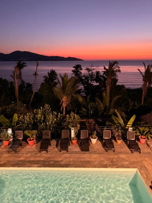 La terrasse piscine de Le Chissioua en bord de mer au coucher du soleil à Sada, avec transats et palmiers dominant l'océan