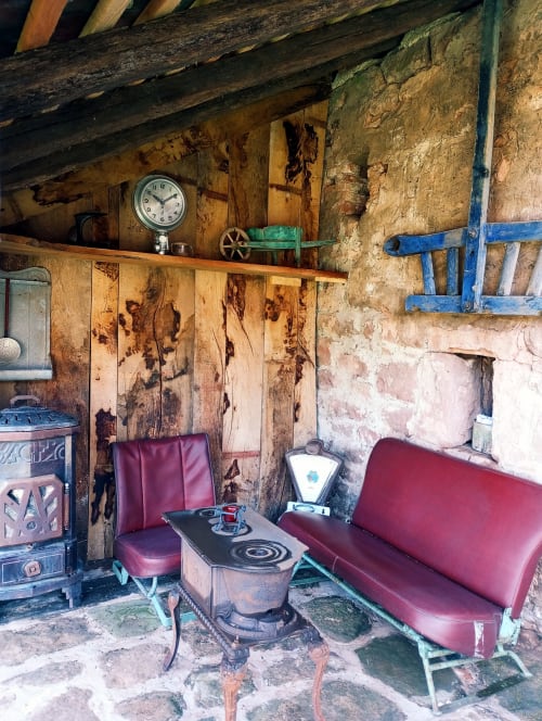 Intérieur rustique de la chambre d'hôtes Paulusmühle à Soucht avec sièges bordeaux, horloge vintage et poutres en bois vieilli