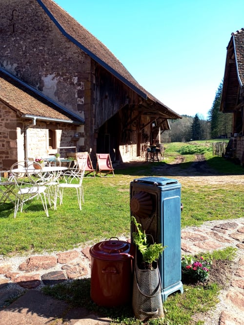 Cour de la Paulusmühle avec poêle vintage, coin détente et bâtiments ruraux français rustiques sous ciel dégagé