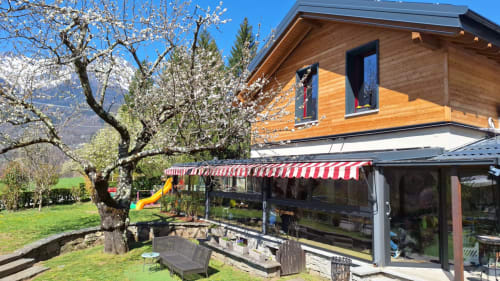 Camere di Locanda del Sasso a Crodo con chalet in legno, veranda ombrellata, albero in fiore e Alpi