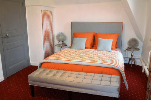 Suite spacieuse au Relais Du Destin avec literie rayée orange et blanc, tête de lit grise et banc crème à Vertrieux