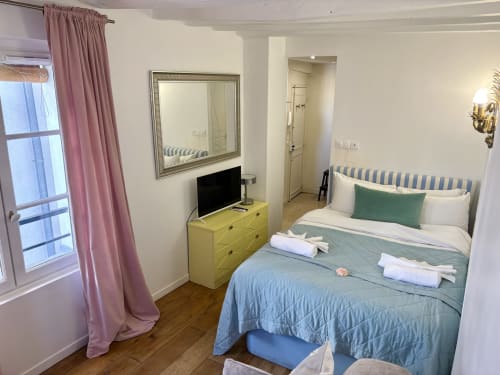 Acogedora habitación de apartamento parisino con cama queen, cómoda amarilla, televisión, cortinas rosas y vistas a la ciudad
