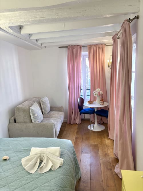 Encantador apartamento parisino con sofá beige, cama, cortinas rosas, pisos de madera y comedor junto a ventanas en el Barrio Latino