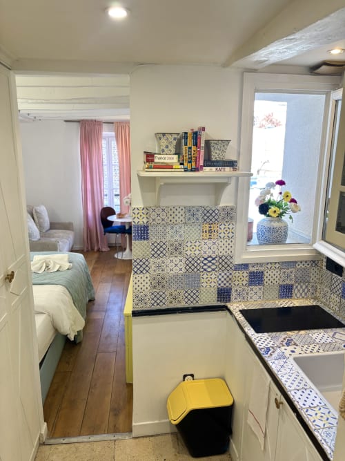 Cocina de apartamento parisino moderno con azulejos estampados azules y blancos, detalles amarillos, dormitorio visible