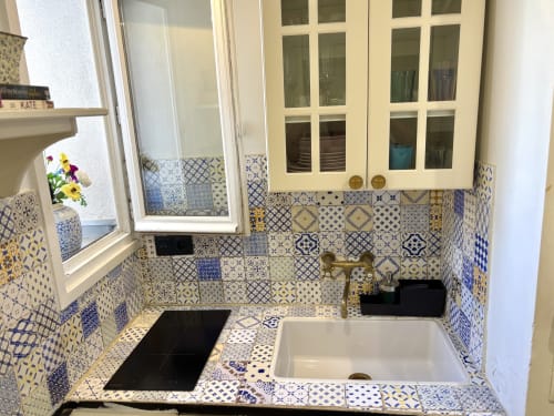 Encantadora cocina parisina con azulejos azules y blancos, muebles blancos y accesorios de latón en el apartamento Aldaro