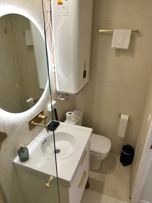 Baño moderno en apartamento parisino con lavamanos blanco, inodoro, espejo, toallero calefactor y calentador de agua