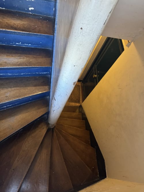 Escalera de caracol con peldaños de madera y barandillas azules en apartamento parisino, pared amarilla visible