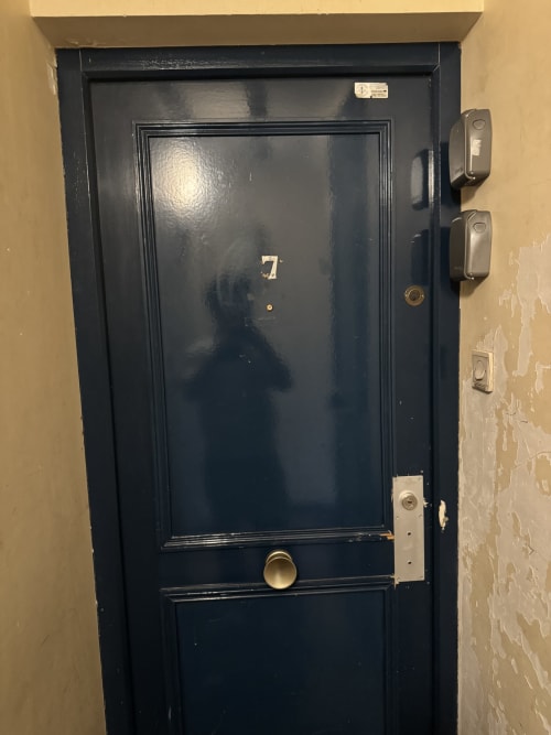 Puerta de apartamento azul oscuro marcada con el número 7 en el hotel Aldaro en el Barrio Latino de París, con caja de llaves e interruptores de luz