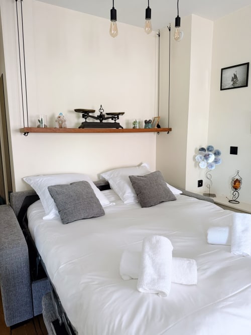 Chambre moderne à la Maison ARLOÉ, La Rochelle avec lit blanc, oreillers gris, étagère en bois et luminaires suspendus
