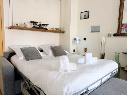 Chambre moderne à la Maison ARLOÉ à La Rochelle avec literie blanche, oreillers gris, étagère en bois et décor vue sur la ville
