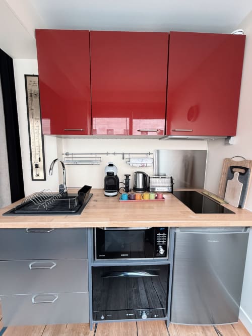 Cuisine moderne aux armoires rouges, appareils en acier inoxydable, comptoir en bois à l'appartement Maison ARLOÉ