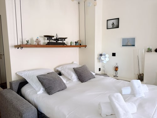 Chambre moderne à la Maison ARLOÉ à La Rochelle avec literie blanche, oreillers gris et décoration nautique sur les étagères.
