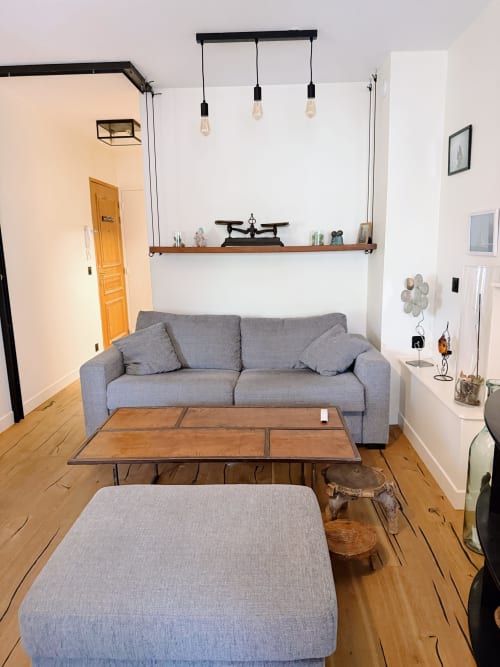 Salon moderne à la Maison ARLOÉ à La Rochelle : canapé gris, tables en bois, luminaires suspendus et étagère murale